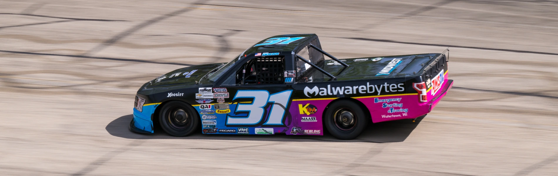 No. 31 black and pink Malwarebytes-sponsored race truck in motion on a concrete oval short track