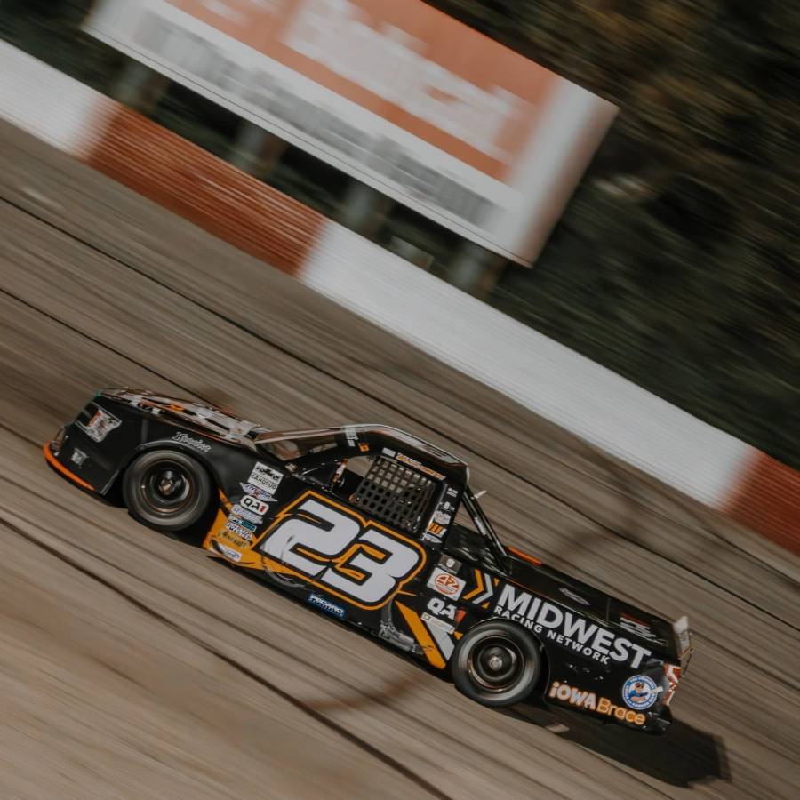 No. 23 black and gold short-track truck race car at speed on a dirt or asphalt oval with Midwest Racing Network and Iowa Brace sponsor graphics